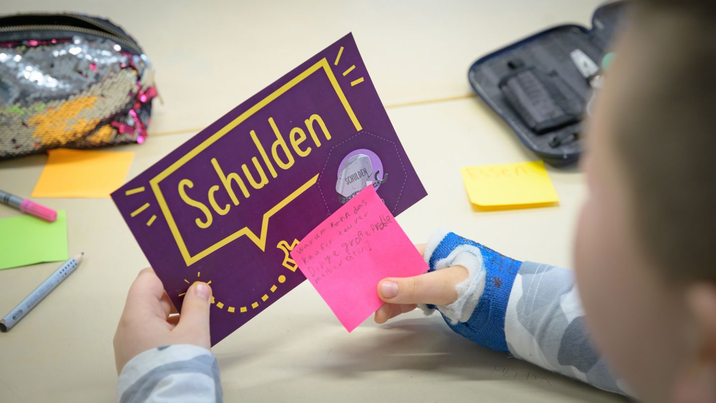 Finanzbildung für Kinder: Kind betrachtet eine Lernkarte zum Thema Schulden.