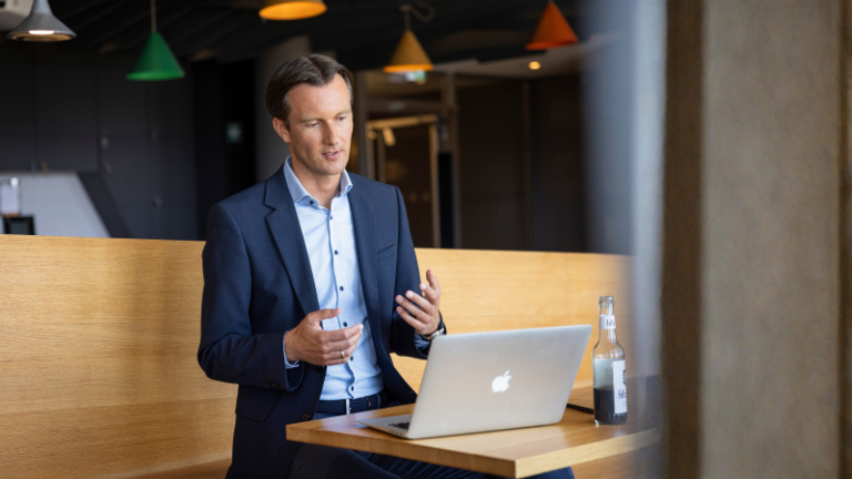 Carsten Tidow sitzt mit aufgeklapptem Laptop auf einer Bank und gestikuliert, während er erklärt.