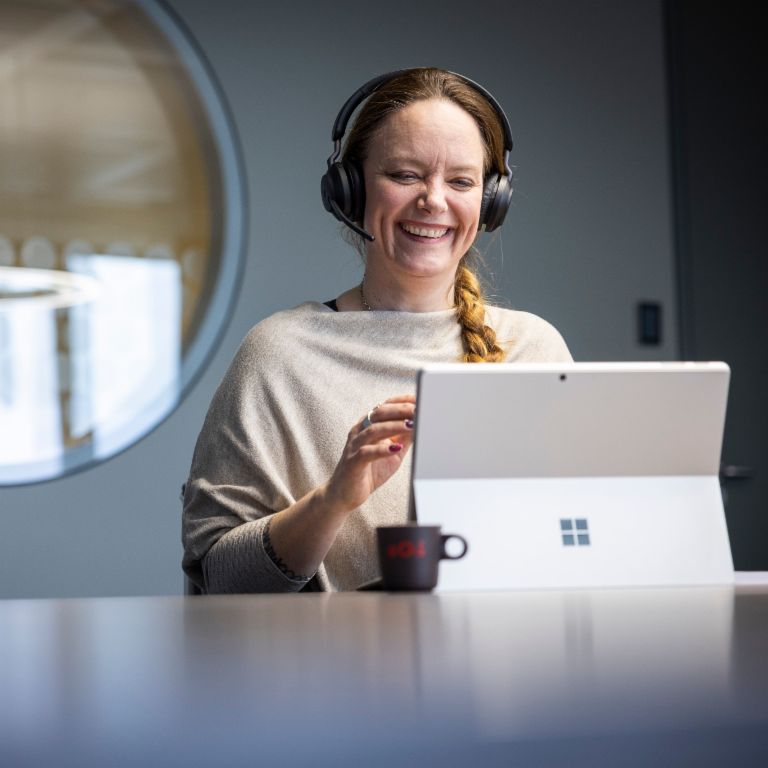 An EOS employee wears a headset and can be seen smiling while conversing with a digital counterpart. There is an EOS espresso cup in front of the computer.
