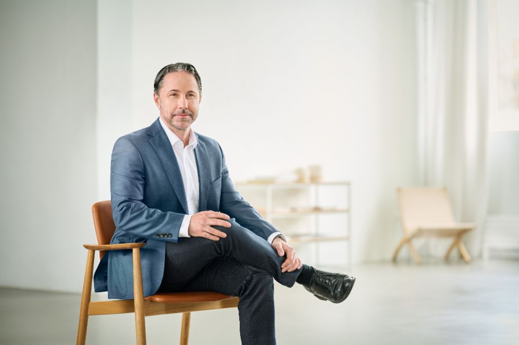Portrait von Marwin Ramcke, Vorsitzender der Geschäftsführung der EOS Gruppe in einem hellen Raum und trägt ein dunkles Sakko