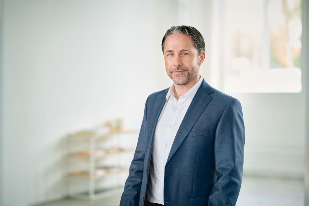 Portrait von Marwin Ramcke, Vorsitzender der Geschäftsführung der EOS Gruppe in einem hellen Raum und trägt ein dunkles Sakko