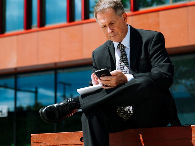 Internationales Inkasso: Raymond Pappot sitzt auf einer Bank und schaut auf sein Smartphone.