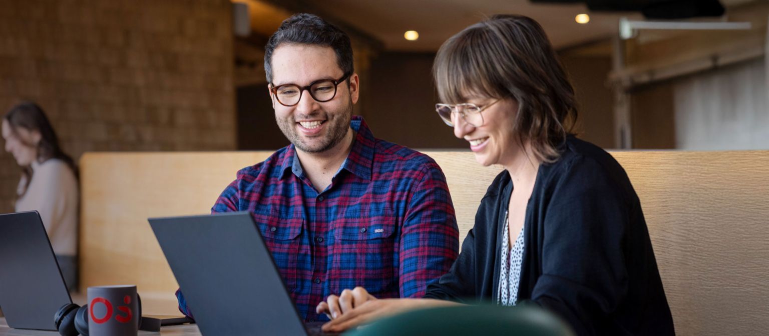 Two EOS employees look at a laptop together while engrossed in a conversation.